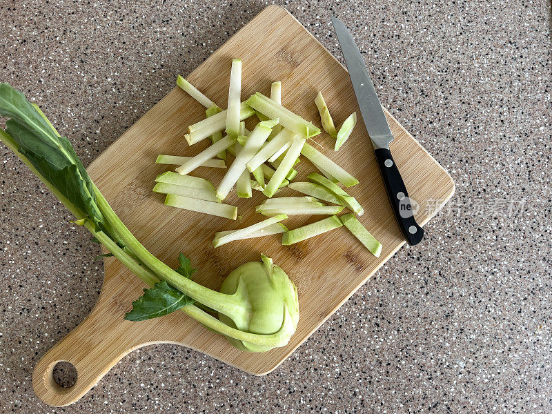 Sliced ​​kohlrabi cabbage, half and cut into strips on a wooden cutting board placed obliquely on a tabletop, top view